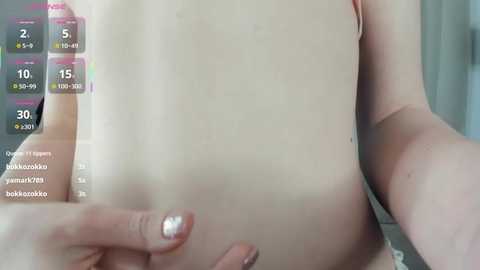 A video shows a close-up of a fair-skinned person's bare chest, with visible nipples and a tattoo on the right breast. The background is blurred.
