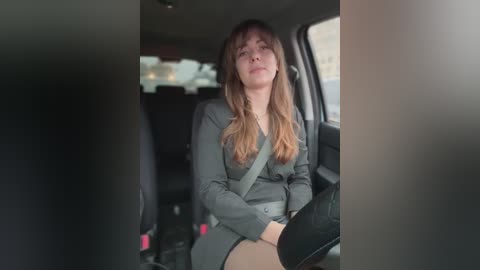 Video of a Caucasian woman with long, light brown hair, wearing a gray suit, sitting in a car, looking relaxed.