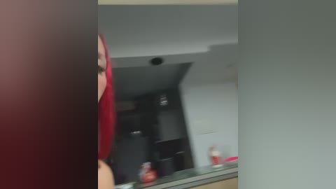 A blurry video of a person in a red shirt standing in a kitchen with a white sink and black appliances.