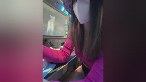 A video of a woman in a VR headset, wearing a pink sweater, operating a computer with a screen displaying a white cat.