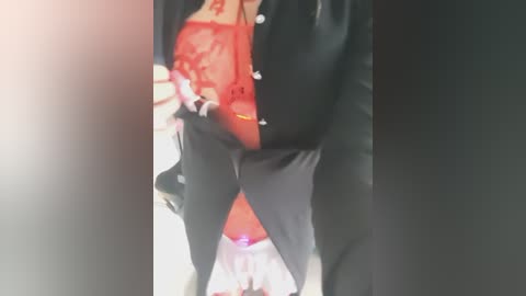 Video of a person wearing a red lace bra, black button-up shirt, and black pants, holding a small, red object.