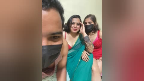 Video: Three South Asian women in traditional sarees, black masks, and red tops; blurred background; one woman has a tattoo on her arm.