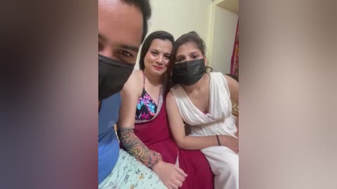 Video of three people in a small room; two women in red and white dresses, wearing masks, and one man in blue.