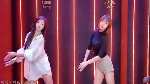 Video of two East Asian women dancing, one in a white robe, the other in a black top and shorts, against a red curtain with Chinese text.