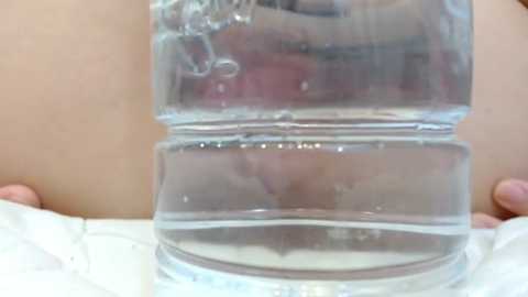 Video of a clear plastic water bottle with a narrow neck, held by two hands on a white surface, displaying its transparent, smooth texture and slight reflections.