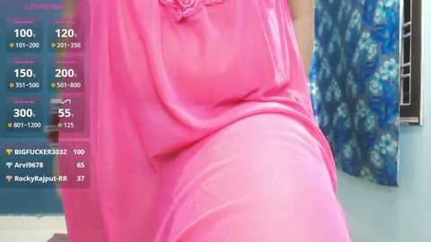 A video showing a woman wearing a pink, loose-fitting dress, with a digital overlay displaying social media metrics. The background features a blue floral patterned curtain and a teal wall.