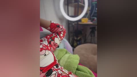 Video of a person in a red and white floral dress, with a green towel draped over their shoulder, in a cozy room with a round mirror and bookshelves.