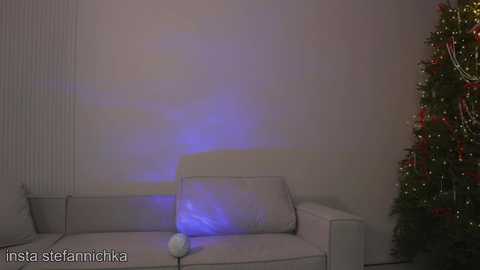 A video of a cozy living room with a white couch and a lit Christmas tree in the corner, emitting soft blue light.