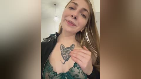 A video of a smiling young woman with light skin and long blonde hair, wearing a black jacket over a green lace bra. She has a detailed wolf tattoo on her chest. The background is blurred.