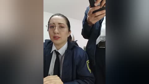 Video of a young woman in a dark blue police uniform, seated, with a neutral expression, taken in a dimly lit room.
