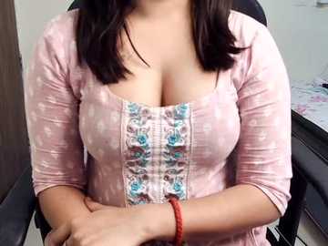 Media: Video of a woman with medium skin tone, wearing a pink blouse with a floral design, showcasing cleavage. She has straight, shoulder-length dark hair and a red bracelet on her wrist.