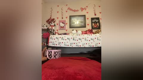 Video of a girly, red-themed bedroom with a bed adorned with heart-shaped pillows, a Hello Kitty pillow, and a \"Valentine's Day\" banner. A plush bear and a teddy bear rest on the bed.