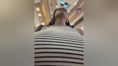 Video of a woman in a black and white striped dress, looking upward, in a modern, brightly lit shopping mall with curved glass ceilings.