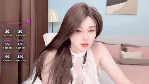 Video of a young Asian woman with long, straight black hair, wearing a white lace top, sitting on a bed with pastel-colored pillows and a beige lampshade in a modern bedroom.