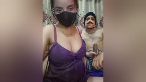 Media: Video of a woman with medium skin tone, black mask, and purple camisole, holding a man's erect penis in a bathroom with floral curtains.