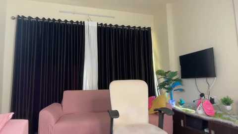 Video of a modern, minimalist living room with beige walls, a large black curtain, a white chair, a pink couch, a flat-screen TV, and a white desk with green plants.