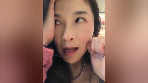 Video of an Asian woman with long black hair, light skin, and red lipstick, playfully touching her own face with a pink feather.