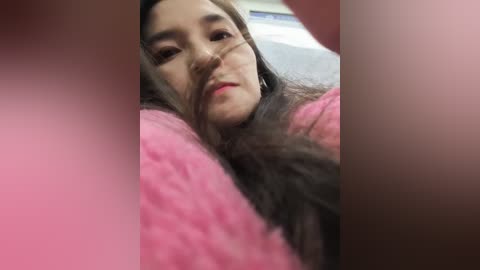 Video of a young Asian woman with long, dark hair, wearing pink clothing, lying on her side, with a blurred background.