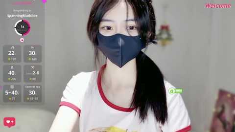 A video of an Asian woman with long black hair, wearing a black mask and white T-shirt, in a home setting with a \"Welcome to Streaming\" overlay.