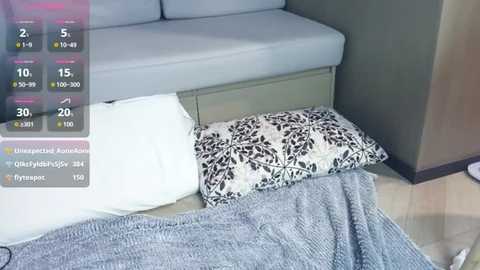 Video of a modern bedroom with a light grey sofa and a patterned pillow, draped in a textured grey blanket, against a green wall. A digital screen overlay shows weather and temperature statistics.