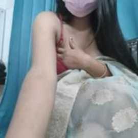 A video of a young woman with long black hair, wearing a red spaghetti strap top, a blue floral-patterned cloth, and a face mask, with a light blue background.