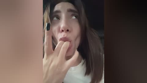 Video of a young Asian woman with light skin, long dark hair, and a distressed expression, being held by a hand with black nails, in a dimly lit room.