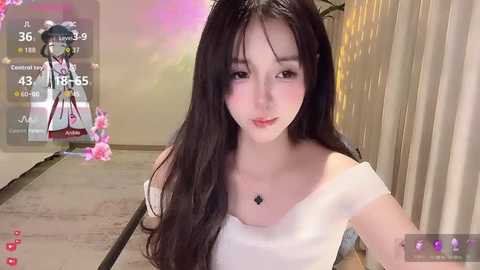 A video of a young Asian woman with long, black hair, fair skin, and a slim physique, wearing a white off-shoulder top. She stands indoors, with a virtual character in the background and a live stream overlay.