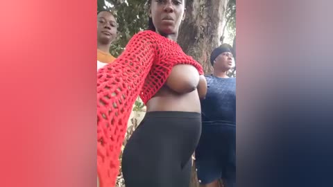 Video of three women in a forest, one in a red crocheted top exposing her large breasts, another in an orange shirt, and the third in a dark outfit.