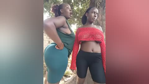 Video of two Black women with dark skin, one in a green tank top and blue shorts, the other in a red mesh top and black leggings, standing outdoors near a tree.