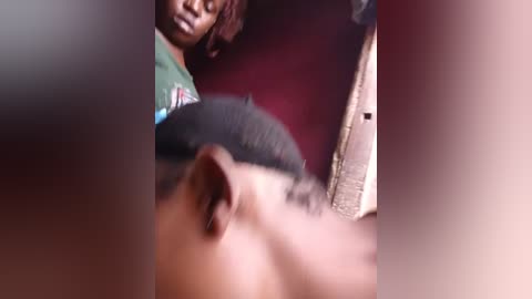 A close-up video showing a person's face with dark hair and medium skin tone, partially blurred, against a blurred red background, suggesting an intimate, possibly tense, indoor setting.