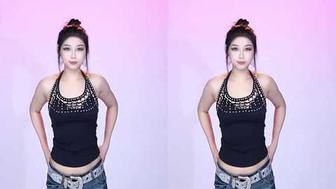 A video of an East Asian woman with light skin and auburn hair styled in a messy bun, wearing a black halter top with intricate white beading and low-rise jeans.