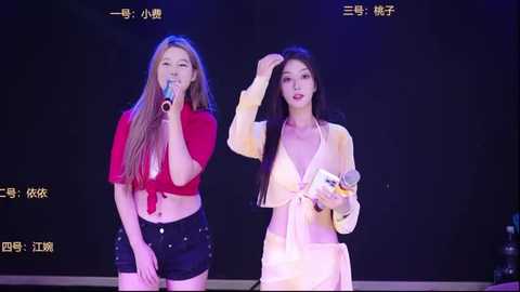 Video of two female singers on stage, one in a red crop top, the other in a yellow cardigan, holding microphones, against a dark background with Chinese text and stage lighting.