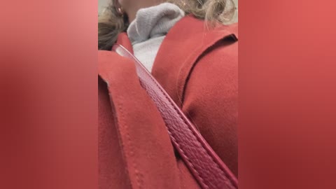 Video of a close-up of a woman wearing a red wool coat over a grey sweater. The focus is on the lapel and shoulder seam, with blurred background.