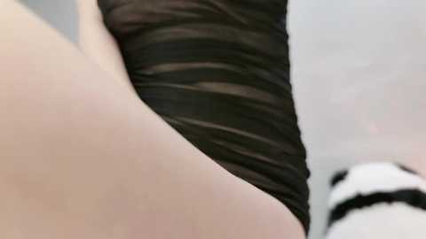 Close-up video of a fair-skinned individual's leg in a sheer black stocking, with a blurred background featuring a white and black striped object, possibly a cat.