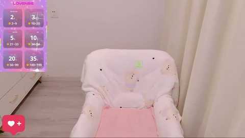 Media: Video of a white highchair with a light pink cushion, adorned with cute bear illustrations, set against a light gray wall and white curtain.