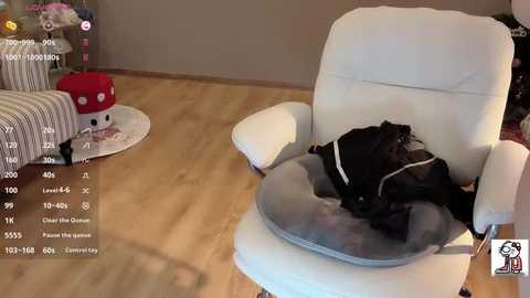 Video of a cozy living room featuring a plush white armchair with a gray blanket, a red mushroom toy, and a striped couch on a light wooden floor.