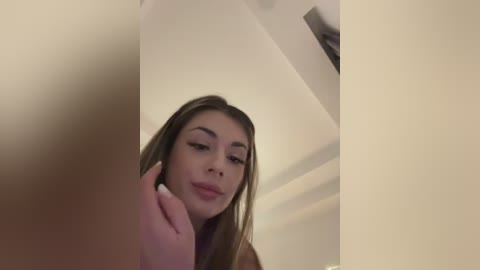 Media: A video of a young woman with long brown hair, light skin, and full lips, taken from a low angle, with a blurred object in the foreground.