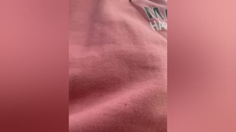 Close-up video of a pale, smooth, slightly wrinkled, and hairless arm, likely male, with part of a gray, \"Mizzou\" shirt visible in the upper right. The background is blurred and pink.