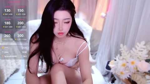 Video of an East Asian woman with long black hair, wearing white lingerie, sitting on a bed, surrounded by white flowers, with live stream stats overlay.