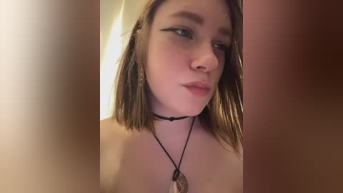 A close-up video of a young Caucasian woman with fair skin and shoulder-length light brown hair, wearing black eyeliner and a choker necklace. The image is slightly blurred and out of focus, with warm lighting.