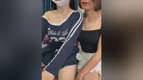Video of two women, one in a blue sweatshirt with white stripes and a face mask, the other in a black strapless dress.