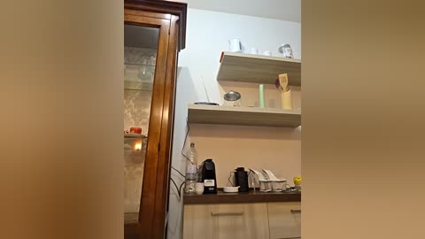 A video of a modern kitchen with light-colored cabinets, open shelves, a microwave, and a coffee maker on a countertop, framed by a large wooden mirror on the left.