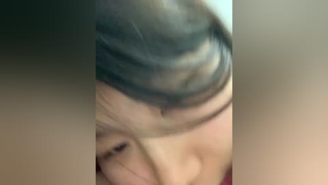 A close-up video of a person's head with short, dark hair, partially obscured by a blurred, light-colored object. The image is slightly out of focus, making it difficult to discern facial features or details.