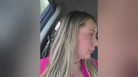 Video of a young Caucasian girl with long, straight blonde hair, wearing a pink shirt, sitting in a car. Her profile is visible, and she's gazing out the window at a blurred background.