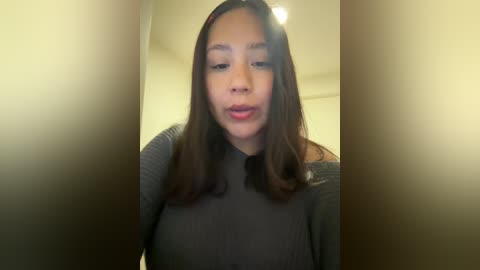 Video of a young Asian woman with long, straight black hair, wearing a gray sweater, indoors with blurred background, slightly out of focus.
