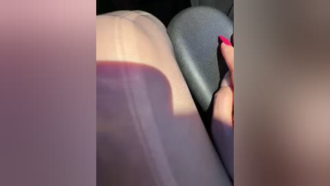 A close-up video of a person's hands and torso, with a focus on their bright red nails. The background features soft, muted colors of grey and beige. The image is blurry, emphasizing texture and color.