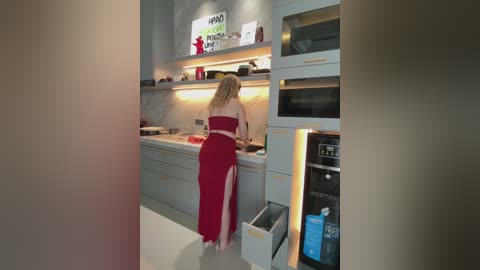 Video of a woman in a red dress cooking in a modern, minimalist kitchen with white cabinets, stainless steel appliances, and a sleek, marble backsplash.