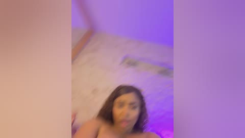 A blurred, out-of-focus video featuring a young woman with medium brown skin and long dark hair, possibly Latina, smiling in a dimly lit room with purple and pink lighting.