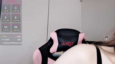 A video of a person wearing a black and pink gaming chair, with a workout tracker displaying stats like calories burned and steps taken, against a plain white wall.