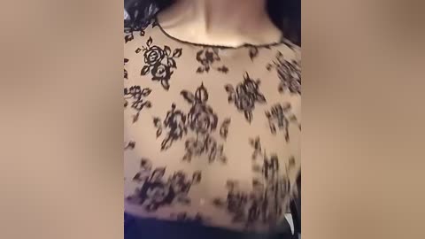 Video of a woman's upper body, wearing a sheer black lace top with floral patterns. Her skin is fair, and her chest is visible through the lace, indicating a light to medium breast size.